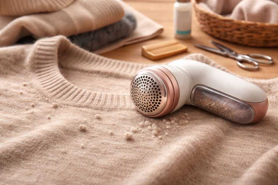 Maglione di lana con pallini in fase di rimozione tramite levapelucchi elettrico su superficie in legno, per la cura e manutenzione dei capi in lana.