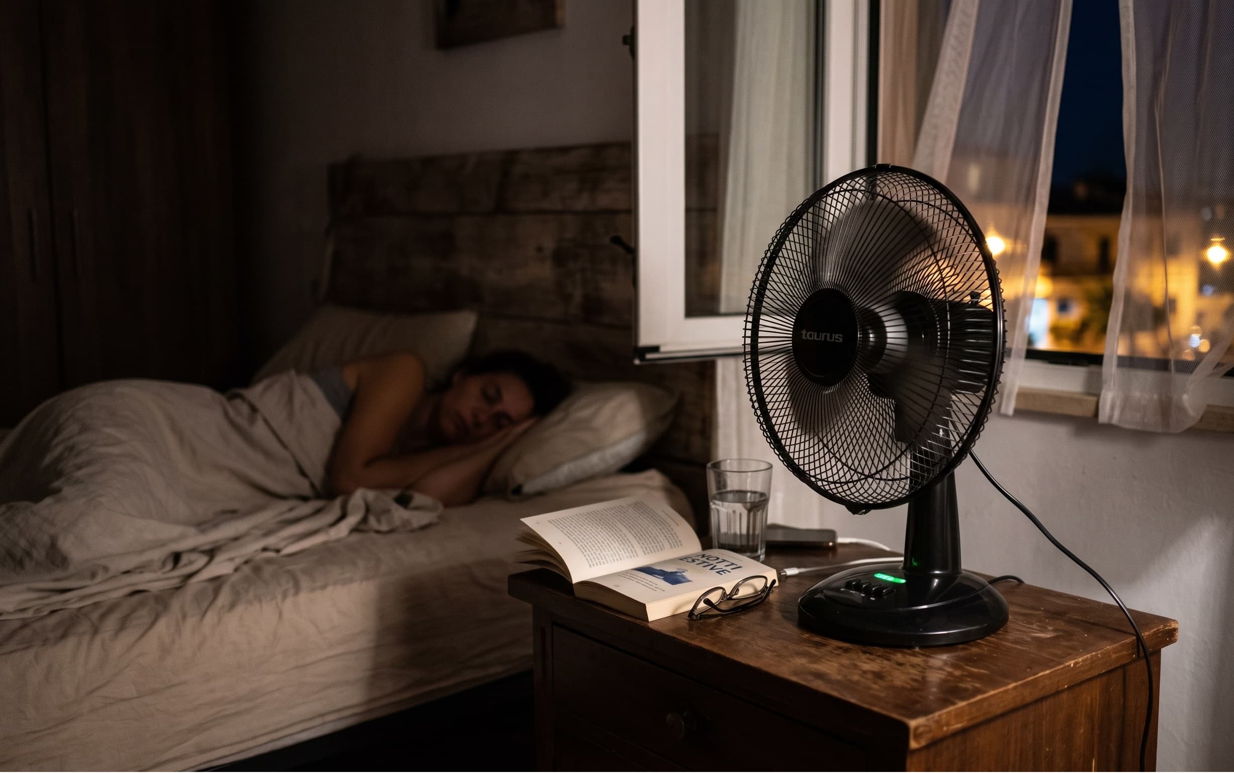 un ventilatore acceso sul comodino di una camera da letto buia in estate