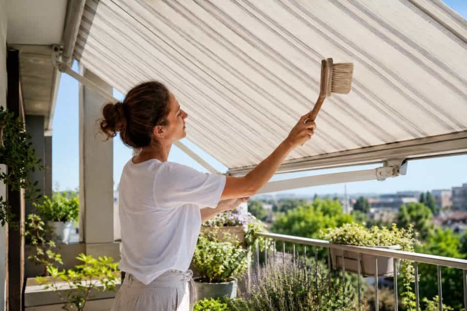 Persona che pulisce delicatamente con una spazzola morbida una tenda da sole aperta sul balcone