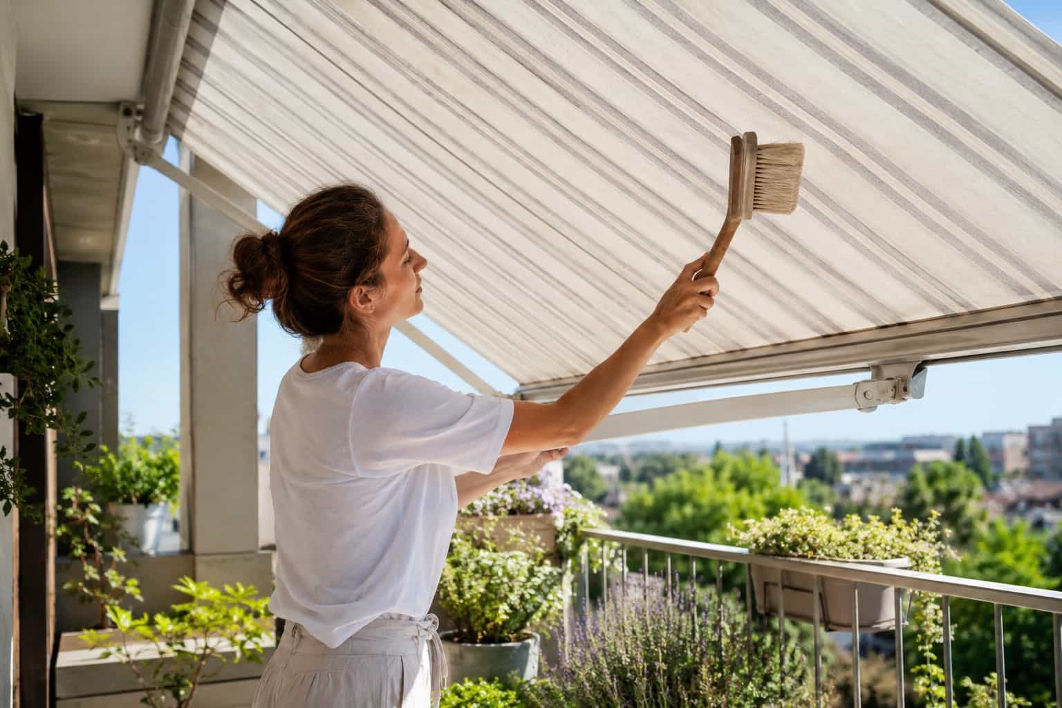 Persona che pulisce delicatamente con una spazzola morbida una tenda da sole aperta sul balcone